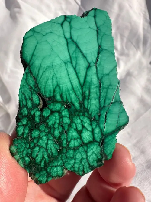 Close-up comparison of rough malachite showing fibrous texture versus polished cabochon